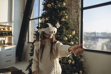 Téléchargez les photos : Le portrait met en scène une belle fille immergée dans la réalité virtuelle, face à un arbre de Noël. Photo de haute qualité - en image libre de droit