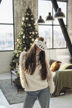 Foto de Una hermosa mujer joven en un auricular de realidad virtual contra el telón de fondo de un árbol de Navidad. Foto de alta calidad - Imagen libre de derechos
