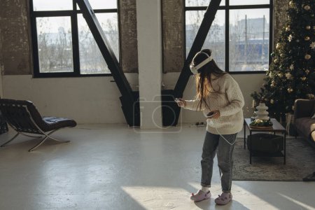 Photo for With sunlight flooding in, an energetic young woman enjoys a virtual reality experience in her apartment. High quality photo - Royalty Free Image