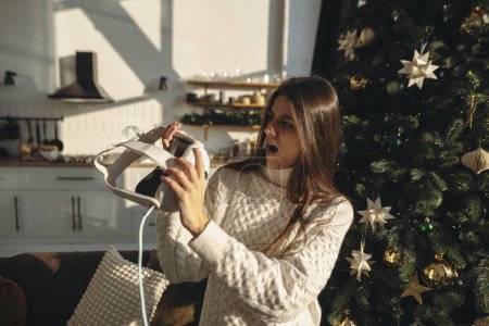Téléchargez les photos : Une jeune femme fougueuse a déballé un casque de réalité virtuelle comme cadeau de Noël. Photo de haute qualité - en image libre de droit