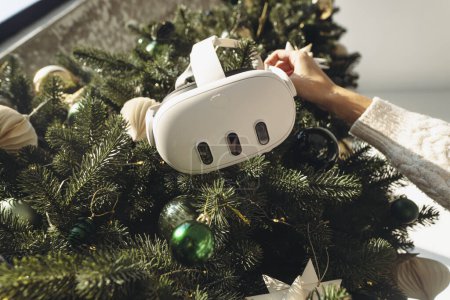 Photo for A girl holds a virtual reality headset against the backdrop of a Christmas tree. High quality photo - Royalty Free Image