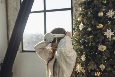 Photo for With sunlight streaming in, a vibrant young woman uses a virtual reality headset on a winter morning. High quality photo - Royalty Free Image