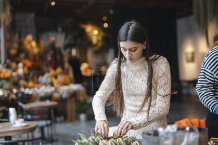 Téléchargez les photos : Les dernières étapes pour compléter la couronne de Noël au comptoir de la boutique de fleurs. Photo de haute qualité - en image libre de droit