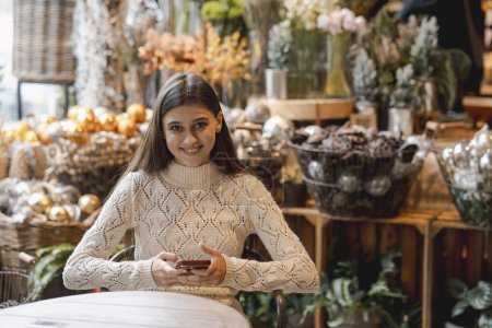 Téléchargez les photos : Dans le magasin de décoration, une jeune femme tient son téléphone. Photo de haute qualité - en image libre de droit