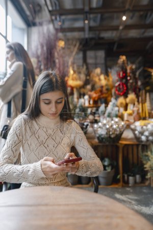 Téléchargez les photos : Avec un téléphone à la main, une jeune femme parcourt la boutique de décoration. Photo de haute qualité - en image libre de droit