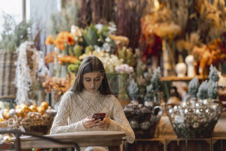 Téléchargez les photos : En explorant le magasin de décoration, une jeune femme tient un téléphone dans ses mains. Photo de haute qualité - en image libre de droit