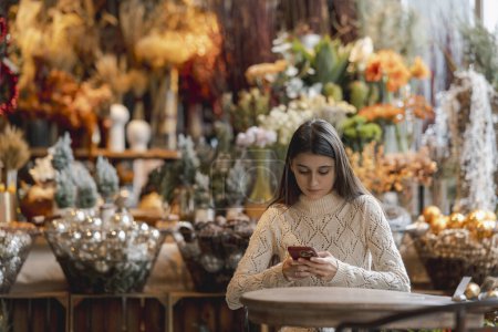 Foto de Una hermosa joven con un teléfono en la mano en la tienda de decoración. Foto de alta calidad - Imagen libre de derechos