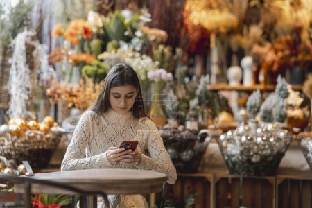 Téléchargez les photos : Une belle femme explore le magasin de décoration avec son téléphone à la main. Photo de haute qualité - en image libre de droit