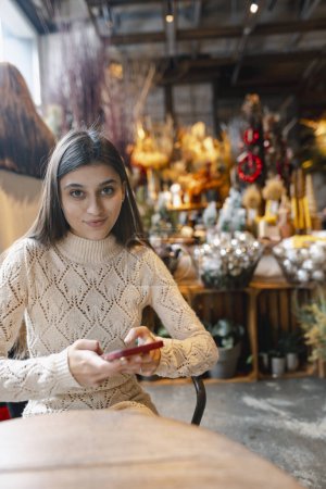 Téléchargez les photos : Une belle femme explore le magasin de décoration avec son téléphone à la main. Photo de haute qualité - en image libre de droit