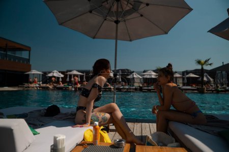 Foto de Un dúo de amigos en traje de baño disfrutan de una tarde tranquila junto a la piscina. Foto de alta calidad - Imagen libre de derechos