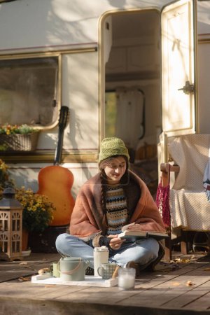 Foto de Una jovencita moderna con un atuendo boho-chic disfruta de una bebida humeante en la terraza. Foto de alta calidad - Imagen libre de derechos