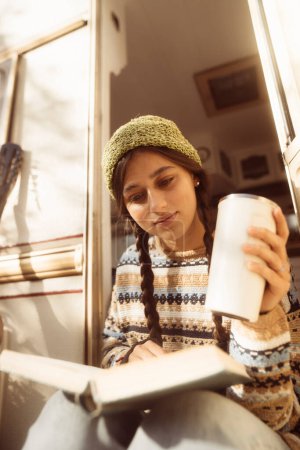 Téléchargez les photos : Une hippie à la mode et contemporaine prend un moment pour savourer une boisson chaude sur la terrasse. Photo de haute qualité - en image libre de droit
