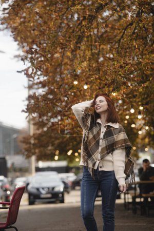 Photo for A merry red-haired girl radiates happiness as she walks through the autumn city streets. High quality photo - Royalty Free Image