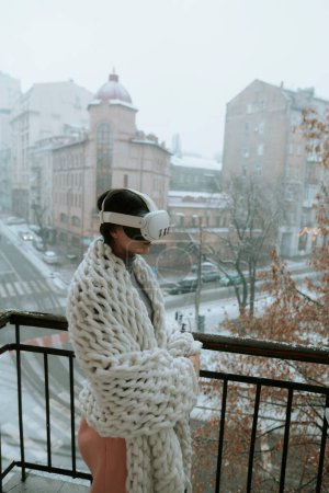 Téléchargez les photos : Une belle fille en lunettes de réalité virtuelle sur fond de paysage urbain hivernal. Photo de haute qualité - en image libre de droit