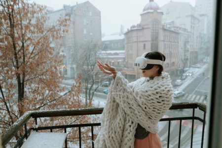 Téléchargez les photos : Une charmante femme en lunettes VR s'émerveille devant la scène hivernale de la ville qui l'entoure. Photo de haute qualité - en image libre de droit