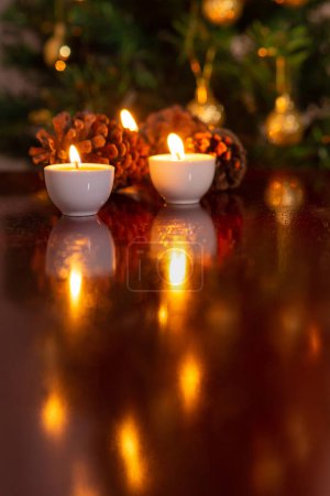 Photo for Christmas decoration. Some lit candles on a reflective surface, and a defocused Christmas tree detail in the background. - Royalty Free Image