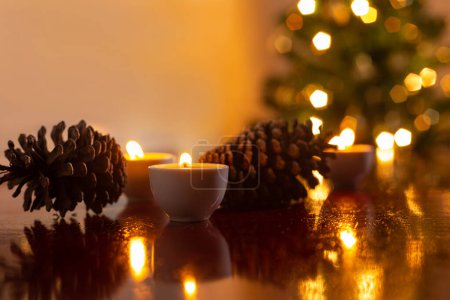 Photo for Christmas decoration. Some lit candles on a reflective surface, two pine cones and a defocused Christmas tree detail in the background. - Royalty Free Image