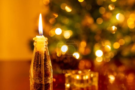 Photo for Christmas decoration. A lit candle in the foreground, and a blurred Christmas tree in the background. - Royalty Free Image
