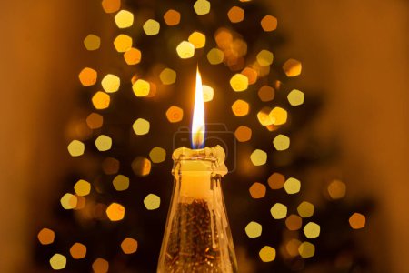 Photo for Christmas decoration. A lit candle in the foreground, and Christmas tree lights glow in the background. - Royalty Free Image