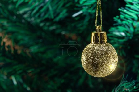Téléchargez les photos : Une boule dorée, suspendue à la branche avec des détails du sapin de Noël en arrière-plan. - en image libre de droit