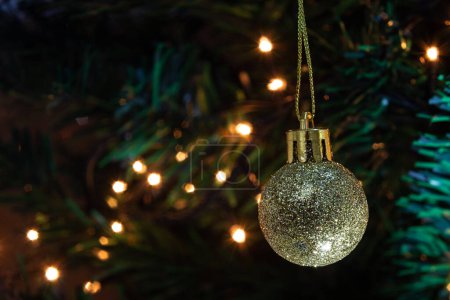 Téléchargez les photos : Une boule dorée, suspendue à la branche avec des détails du sapin de Noël et des lumières en arrière-plan. - en image libre de droit