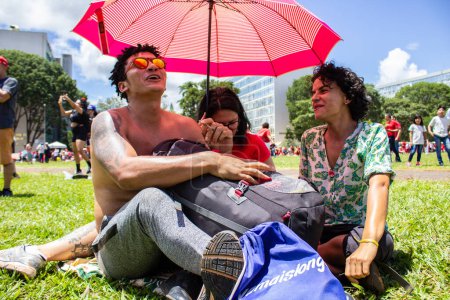 Foto de Tres personas protegiéndose del sol con un paraguas. Foto tomada en el acto de inauguración del nuevo presidente de Brasil. - Imagen libre de derechos