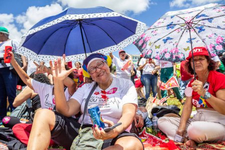 Foto de Dos mujeres sentadas en el suelo, protegiéndose del sol caliente con sombrillas de colores. Foto tomada durante la fiesta de inauguración del presidente Lula. - Imagen libre de derechos