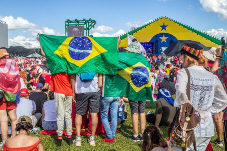 Foto de Supporters of President Lula, using flags to protect themselves against the hot sun and accompanying the inaugural speech of the president-elect. Photo taken at the inauguration event of the new president of Brazil. - Imagen libre de derechos