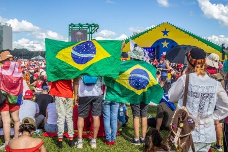Foto de Supporters of President Lula, using flags to protect themselves against the hot sun and accompanying the inaugural speech of the president-elect. Photo taken at the inauguration event of the new president of Brazil. - Imagen libre de derechos