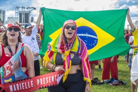 Foto de Two women with a banner written "Marielle, present!" and with a big Brazilian flag in the background. Inauguration event of the new president of Brazil. - Imagen libre de derechos