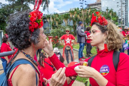 Foto de Una mujer que aplica purpurina en la cara de otra mujer. Foto tomada durante el acto de inauguración del Presidente de Brasil. - Imagen libre de derechos