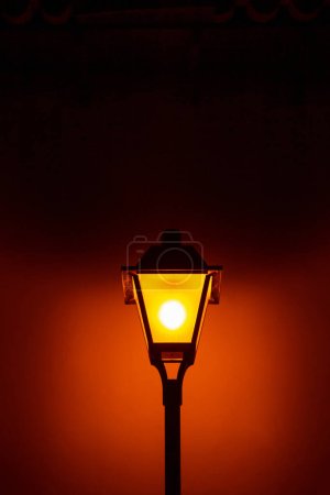 A pole with a vintage street light, lit, at night.