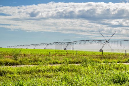 Téléchargez les photos : Machine d'irrigation arrosant la culture, par temps clair avec quelques nuages dans le ciel. - en image libre de droit