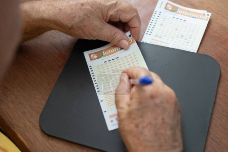 Téléchargez les photos : Gros plan sur les mains d'un homme âgé qui marque les numéros sur une carte de jeu de loterie. - en image libre de droit
