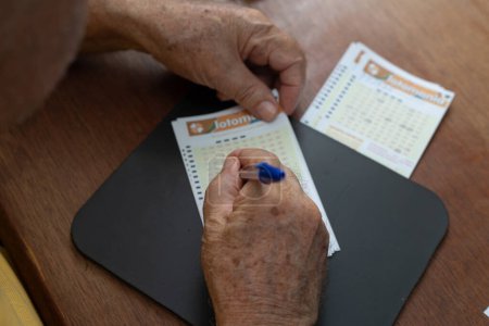 Téléchargez les photos : Gros plan sur les mains d'un homme âgé qui marque les numéros sur une carte de jeu de loterie. - en image libre de droit