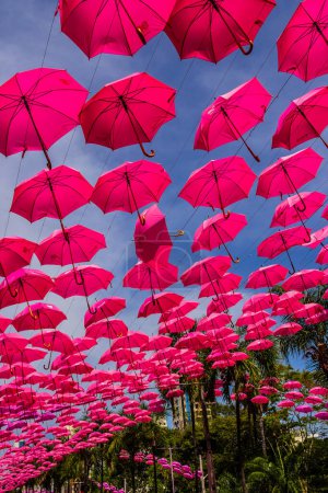 Photo for Several open pink umbrellas, hanging by threads, with the sky in the background. Breast cancer awareness campaign. - Royalty Free Image