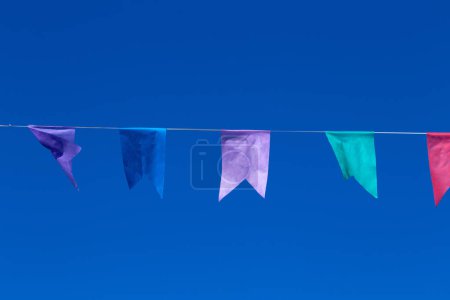 A string with several colorful flags hanging with blue sky in the background. With space to write.
