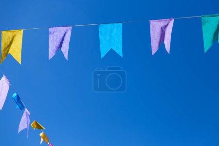  Two strings with colorful flags hanging with blue sky in the background. With space for text.