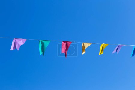 A string of colorful flags hangs, waving in the wind, with the blue sky in the background. With space for text.