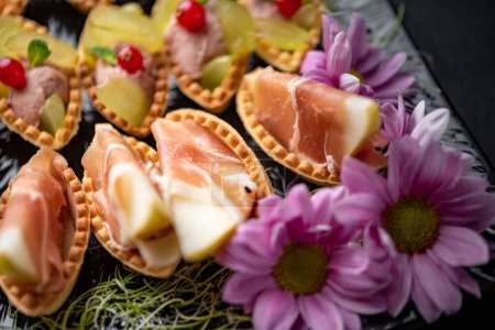 Foto de Canapés con jamón, bayas y puré de verduras servidos con flores - Imagen libre de derechos