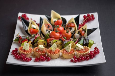 Téléchargez les photos : Plat de fête avec entrées de fruits de mer et de fromage, légumes grillés et groseilles rouges - en image libre de droit