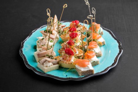Téléchargez les photos : Entrées gourmandes de fruits de mer avec saumon, poisson fermenté, poulpe, fromage à la crème et fraises servies sur assiette bleue - en image libre de droit