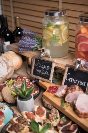 Foto de Set de elegantes aperitivos servidos en mesa de estilo rústico con limonadas y alcohol - Imagen libre de derechos