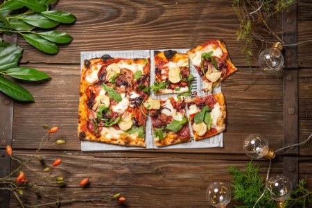 Téléchargez les photos : Vue de dessus de pizza tranchée servie sur table avec branches d'arbres et guirlande - en image libre de droit