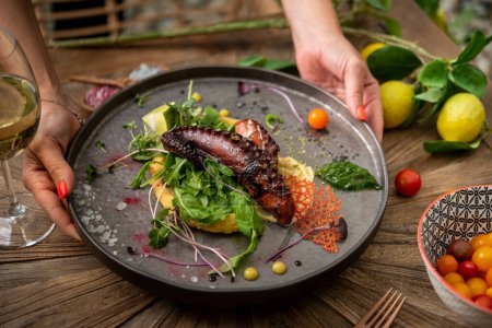 Téléchargez les photos : Serveuse servant pieuvre grillée avec vin blanc sur table en bois - en image libre de droit