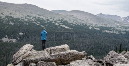 Photo for Single Person In Blue Coat Stands On Rocks overlooking Stormy Peaks Pass - Royalty Free Image
