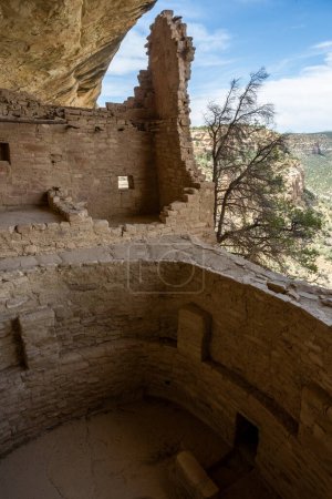 Foto de Gran Kiva y la pared de piedra restante en el borde de la casa de balcón en el Parque Nacional Mesa Verde - Imagen libre de derechos