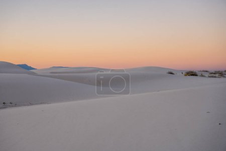 Les dunes lisses se fondent les unes dans les autres contre les couleurs du coucher du soleil dans le parc national White Sands