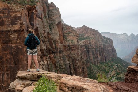 Frau steht auf Felsvorsprung und blickt an bedecktem Tag über den Zion Canyon
