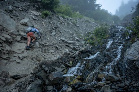 Wanderer erklimmt felsiges Ufer des Creek in Richtung Gletscherwiesen im Olympic National Park
